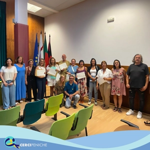 Grupo de pessoas colaboradoras da Cercipeniche, junto a formadores em cerimonia de entrega de certificados RVCC. Logotipos e elemento gráfico.