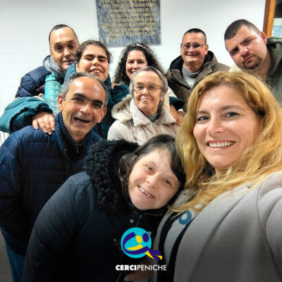 Grupo de pessoas apoiadas pela Cercipeniche posa com a animadora Raquel durante ensaio do rancho folclórico em Geraldes. Logo da Cercipeniche.