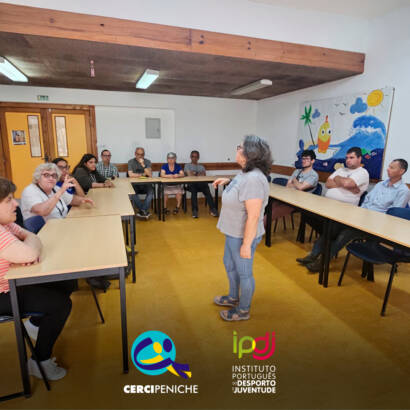 Fotografia da sala de formação durante a sessão sobre convulsões. Ao fundo da sala, várias pessoas apoiadas assistem à apresentação da enfermeira Cristina Costa. Logo da Cercipeniche.