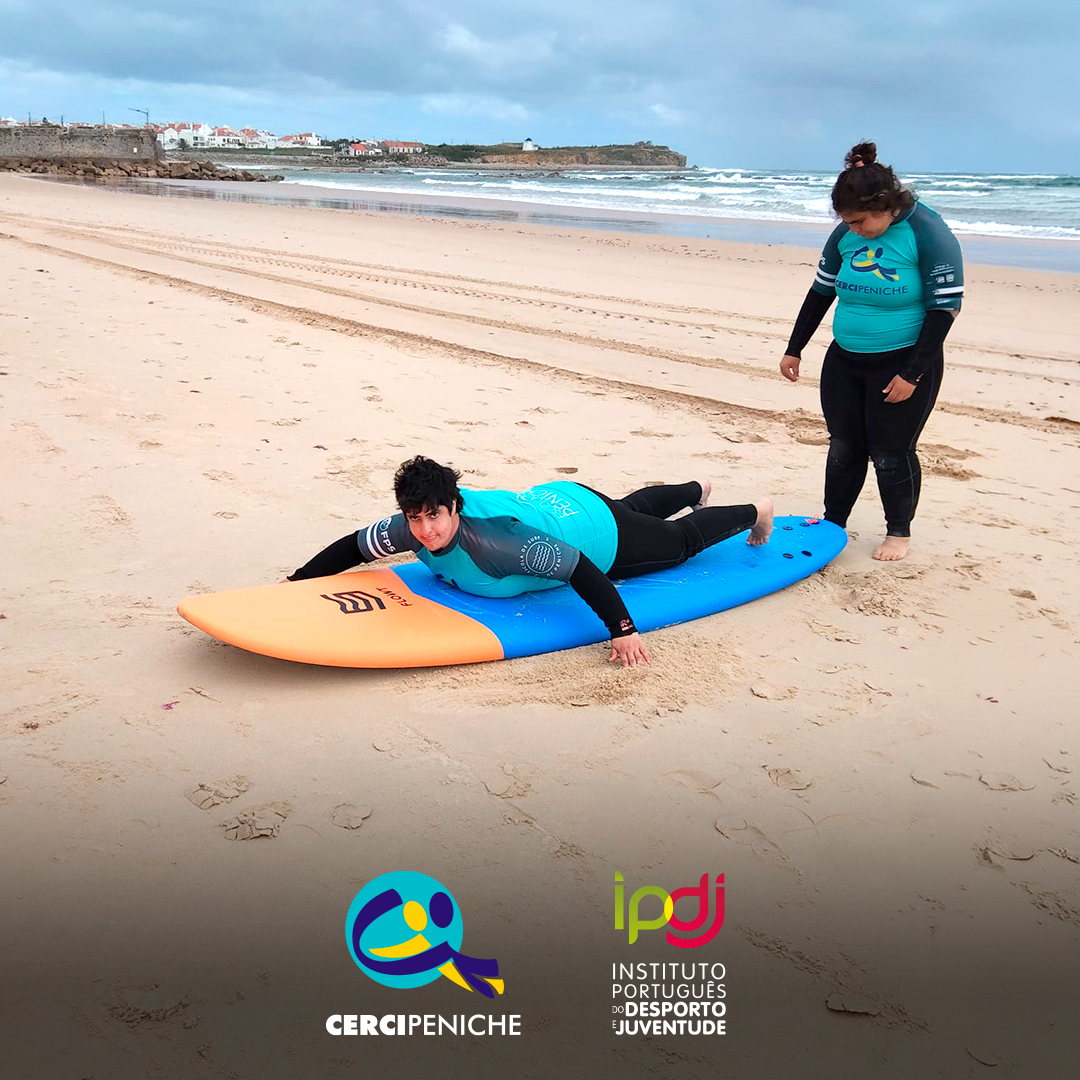 Pessoas apoiadas pela Cercipeniche em treino de equilíbrio sobre a prancha de surf, em aquecimento antes da prática no mar. Logo da Cercipeniche.