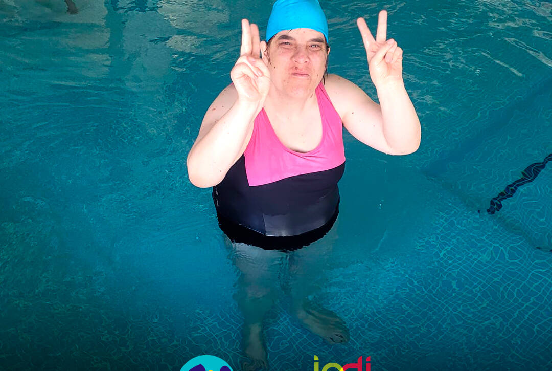 Pessoa apoiada pela Cercipeniche dentro da piscina, a posar para a foto durante a aula de natação. Logo da Cercipeniche e do IPDJ.