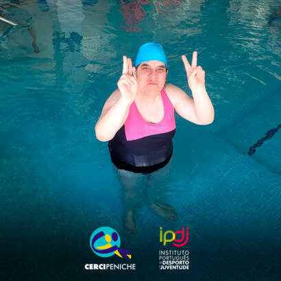 Pessoa apoiada pela Cercipeniche dentro da piscina, a posar para a foto durante a aula de natação. Logo da Cercipeniche e do IPDJ.