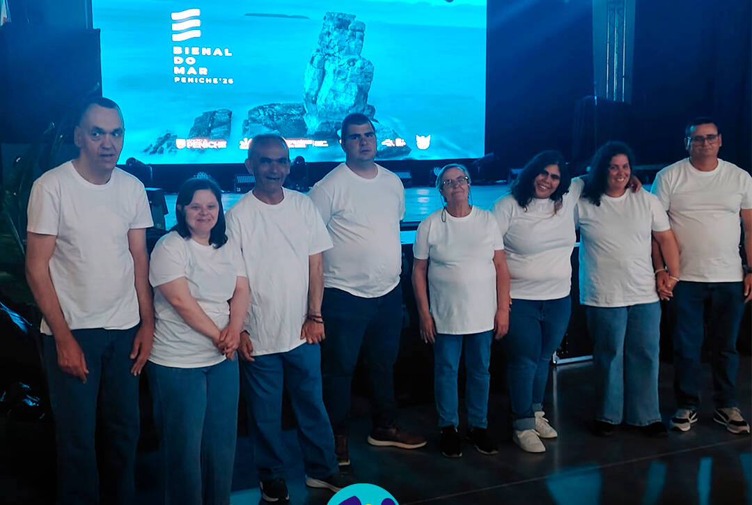 Fotografia de grupo com as pessoas apoiadas pela Cercipeniche antes da sua atuação na Bienal do Mar em Peniche. Logótipo da Cercipeniche.