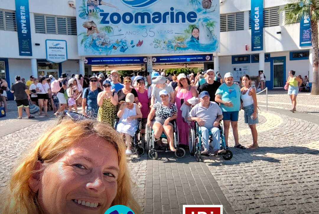 Grupo de pessoas apoiadas e monitores da Cercipeniche à entrada do Zoomarine, no Algarve. Logótipo da Cercipeniche e do IDiPD.