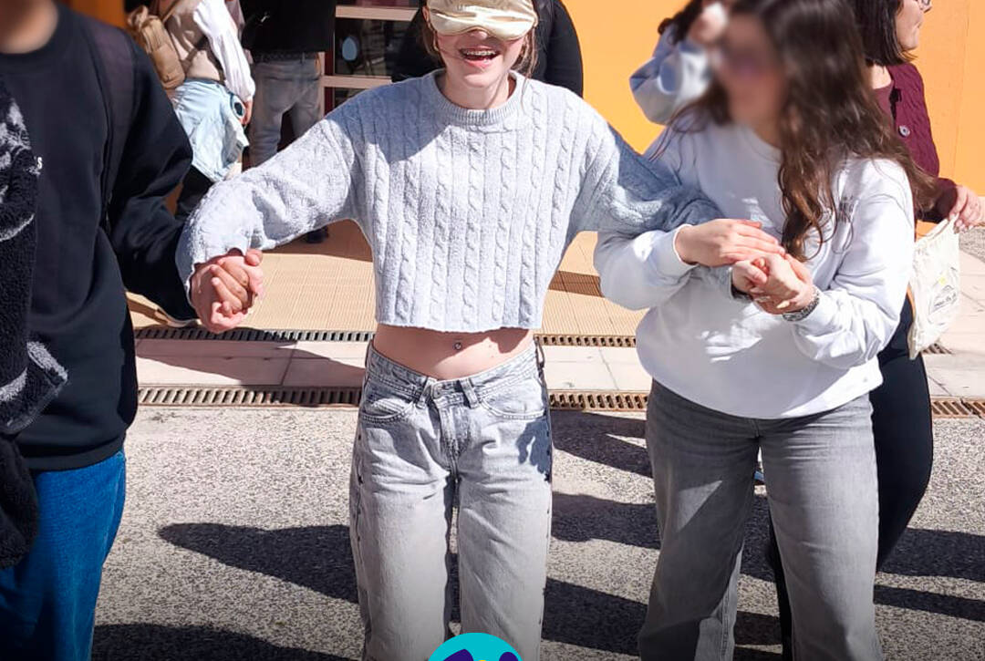 Aluna vendada, apoiada por colegas, durante uma atividade de sensibilização na Feira da Saúde. Logo da Cercipeniche.