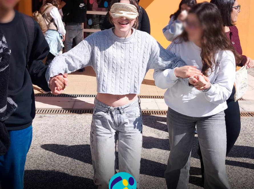 Aluna vendada, apoiada por colegas, durante uma atividade de sensibilização na Feira da Saúde. Logo da Cercipeniche.