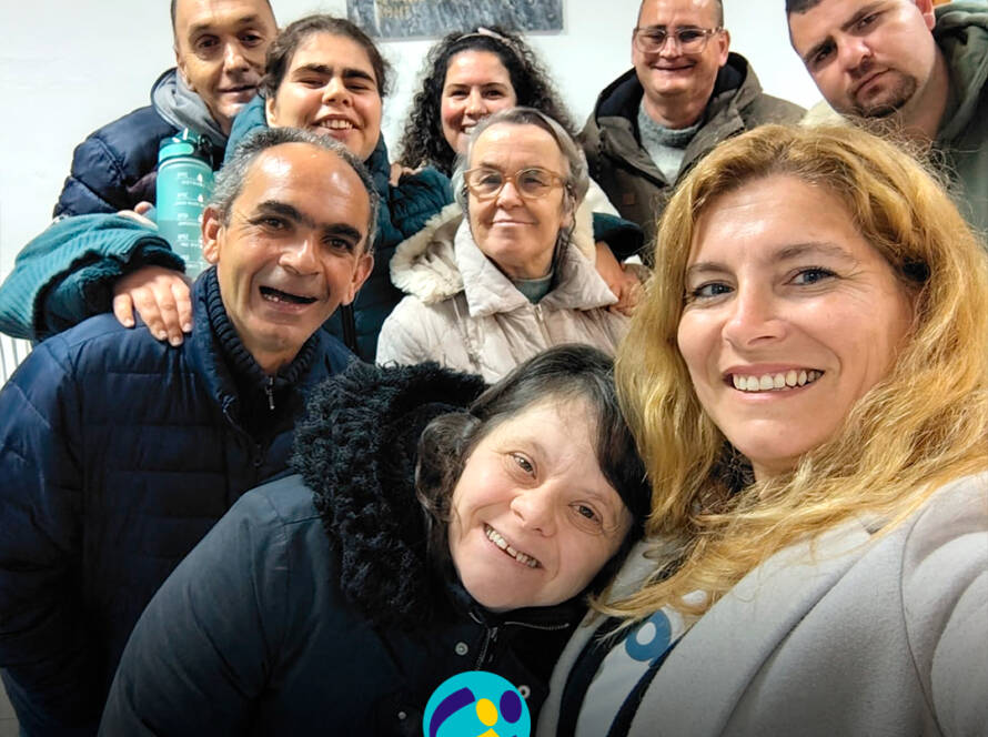 Grupo de pessoas apoiadas pela Cercipeniche posa com a animadora Raquel durante ensaio do rancho folclórico em Geraldes. Logo da Cercipeniche.