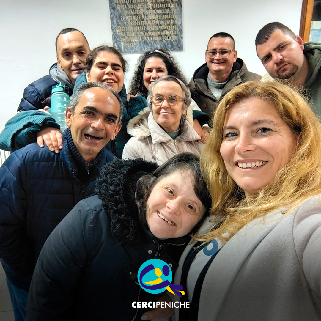 Grupo de pessoas apoiadas pela Cercipeniche posa com a animadora Raquel durante ensaio do rancho folclórico em Geraldes. Logo da Cercipeniche.