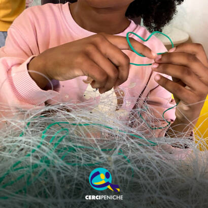 Mãos de uma criança a explorar redes de pesca no Atelier das Redes. Logo da Cercipeniche.
