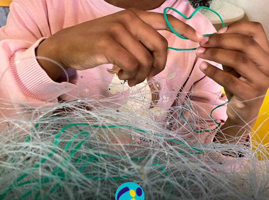 Mãos de uma criança a explorar redes de pesca no Atelier das Redes. Logo da Cercipeniche.