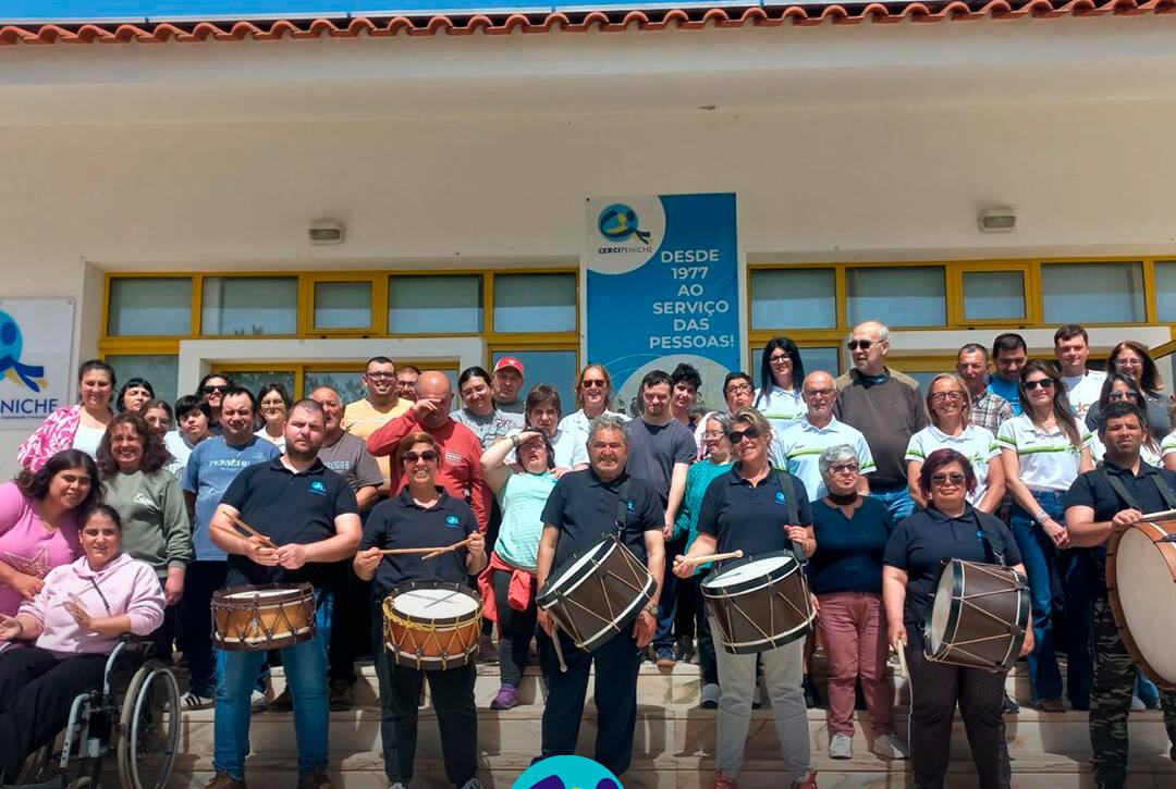 Pessoas apoiadas e colaboradores da Cercipeniche, juntamente com as representantes da associação Peniche a Correr, posam em grupo com os bombos e a tarolas oferecidos. Logo da Cercipeniche.