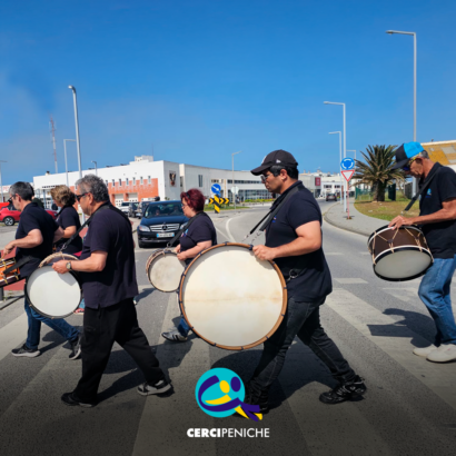 Grupo de pessoas apoiadas a tocar bombos na rua, durante o evento EnREDES. Logo da Cercipeniche.