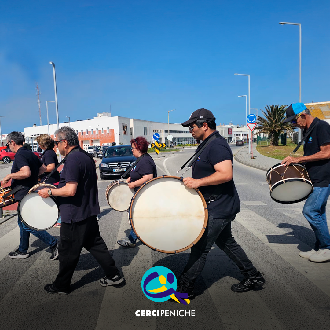 Grupo de pessoas apoiadas a tocar bombos na rua, durante o evento EnREDES. Logo da Cercipeniche.
