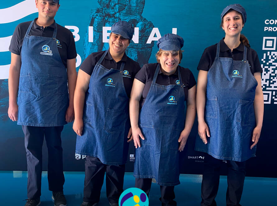Grupo de participantes pousam para a foto, felizes, antes do início da atividade na Bienal do Mar. Logo da Cercipeniche.