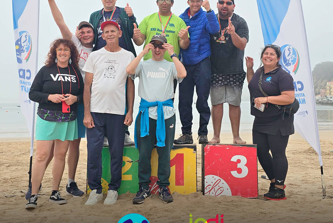 Foto na praia, com o grupo de pessoas apoiadas pela Cercipeniche e monitoras, no pódio. Logos da Cercipeniche e do IPDJ.