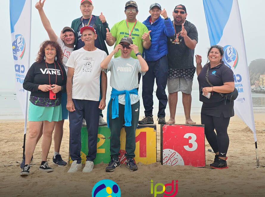 Foto na praia, com o grupo de pessoas apoiadas pela Cercipeniche e monitoras, no pódio. Logos da Cercipeniche e do IPDJ.