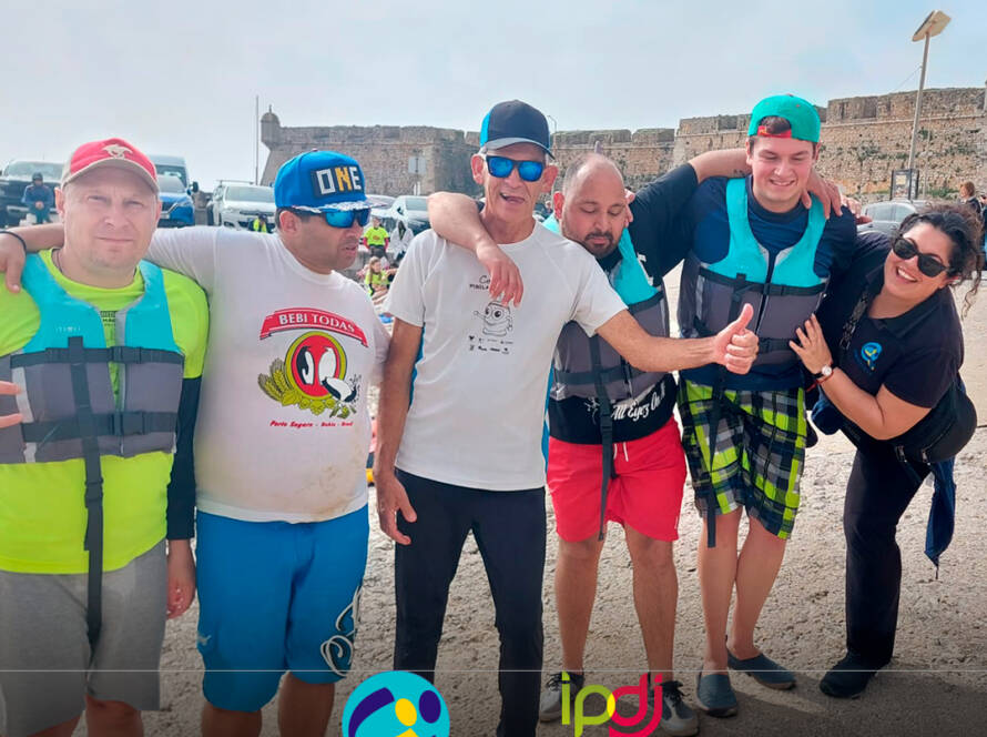 Grupo de pessoas apoiadas pela Cercipeniche, na Marina de Peniche, antes da atividade aquática. Logótipos da Cercipeniche e do IPDJ.