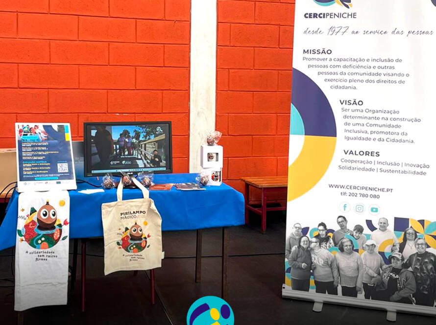 Mesa com materiais informativos da Cercipeniche - poster e flyers com as nossas formações, IRS solidário e evento Sunset Pirilampo Mágico, e produtos Pirilampo Mágico à venda. À direita, o nosso Roll Up indtitucional. Logo da Cercipeniche.
