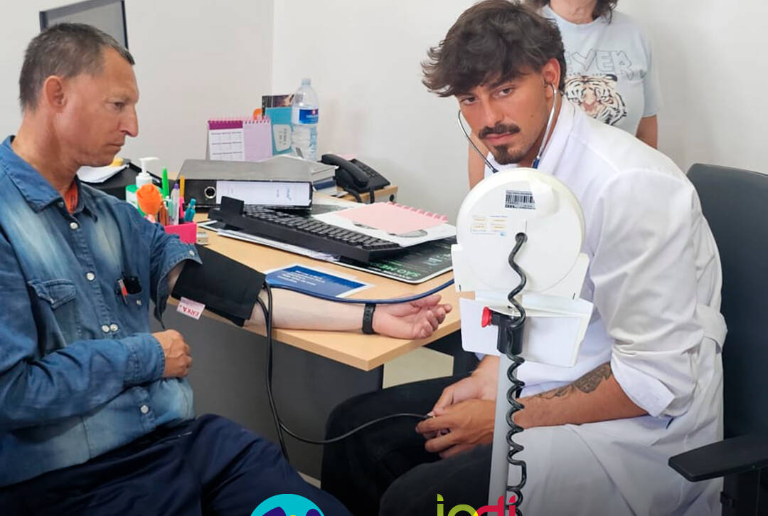 Médico a realizar a medição da tensão arterial a uma pessoa apoiada. Logo da Cercipeniche e do IPDJ.