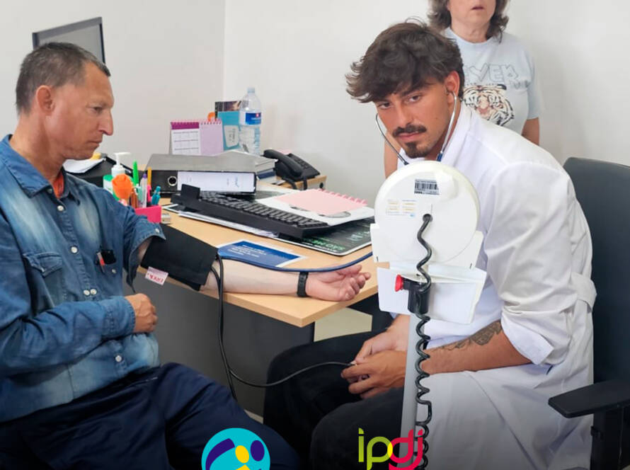 Médico a realizar a medição da tensão arterial a uma pessoa apoiada. Logo da Cercipeniche e do IPDJ.