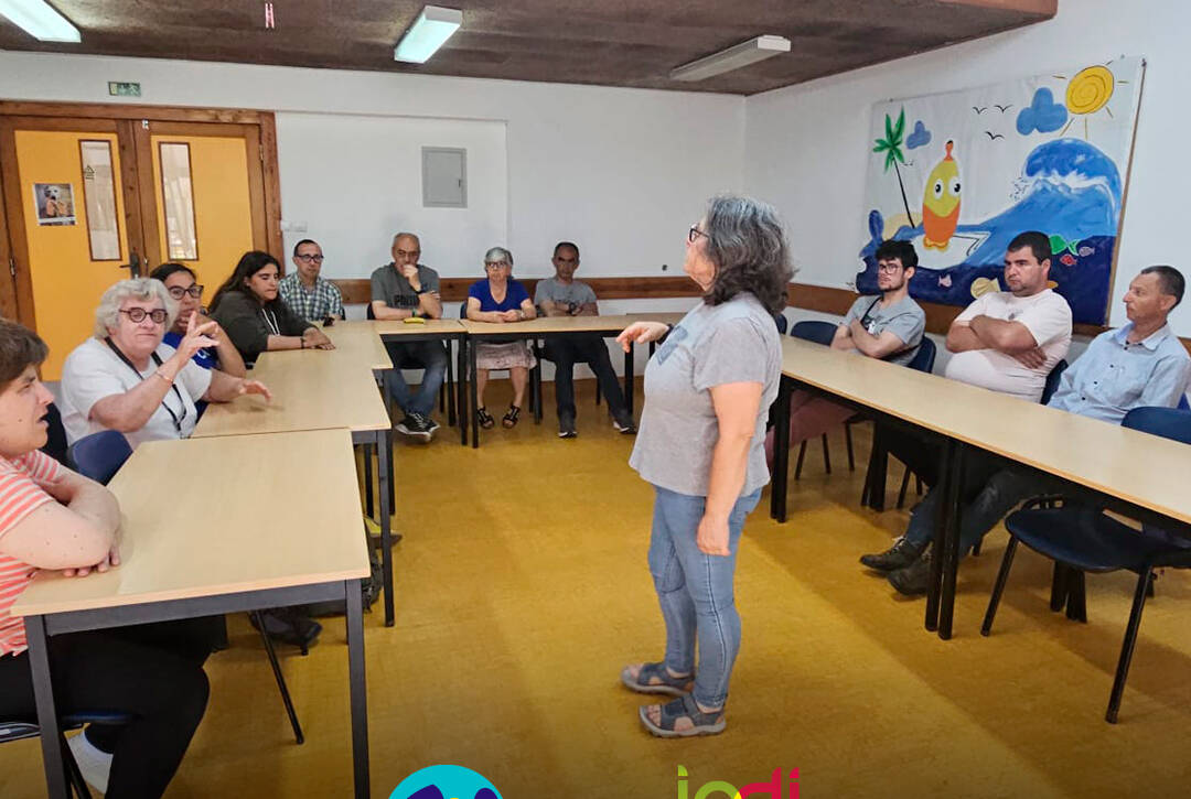 Fotografia da sala de formação durante a sessão sobre convulsões. Ao fundo da sala, várias pessoas apoiadas assistem à apresentação da enfermeira Cristina Costa. Logo da Cercipeniche.