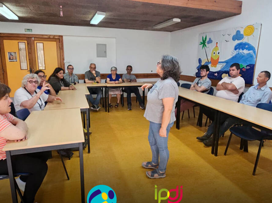 Fotografia da sala de formação durante a sessão sobre convulsões. Ao fundo da sala, várias pessoas apoiadas assistem à apresentação da enfermeira Cristina Costa. Logo da Cercipeniche.