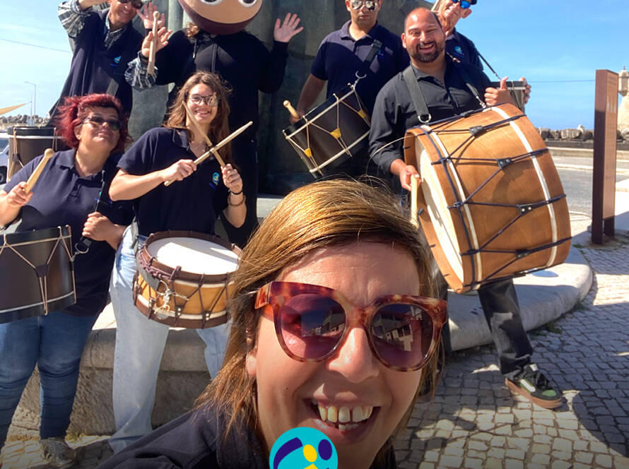 Grupo de Bombos da Cercipeniche pousam para a foto junto à estátua do Pescador, ao pé da ribeira. Logo da Cercipeniche.