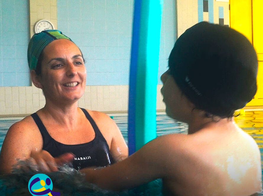 CRI – Centro de Recursos para a Inclusão: Técnica da Cercipeniche sorri enquanto acompanha um menino numa atividade realizada dentro da piscina. Logo da Cercipeniche.