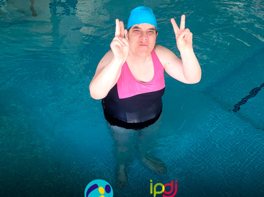 Pessoa apoiada pela Cercipeniche dentro da piscina, a posar para a foto durante a aula de natação. Logo da Cercipeniche e do IPDJ.