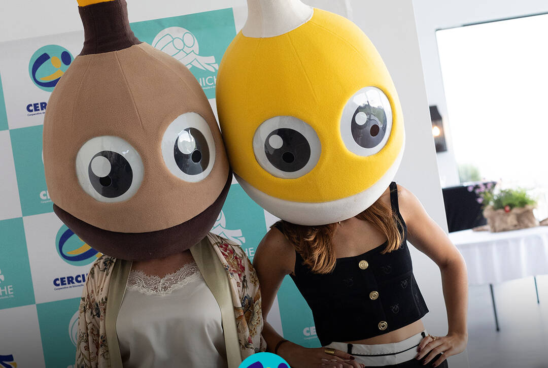 Pessoas com as mascotes do Pirilampo Mágico na cabeça, o castanho e o amarelo, durante o evento Sunset Pirilampo Mágico `26. Logo da Cercipeniche.