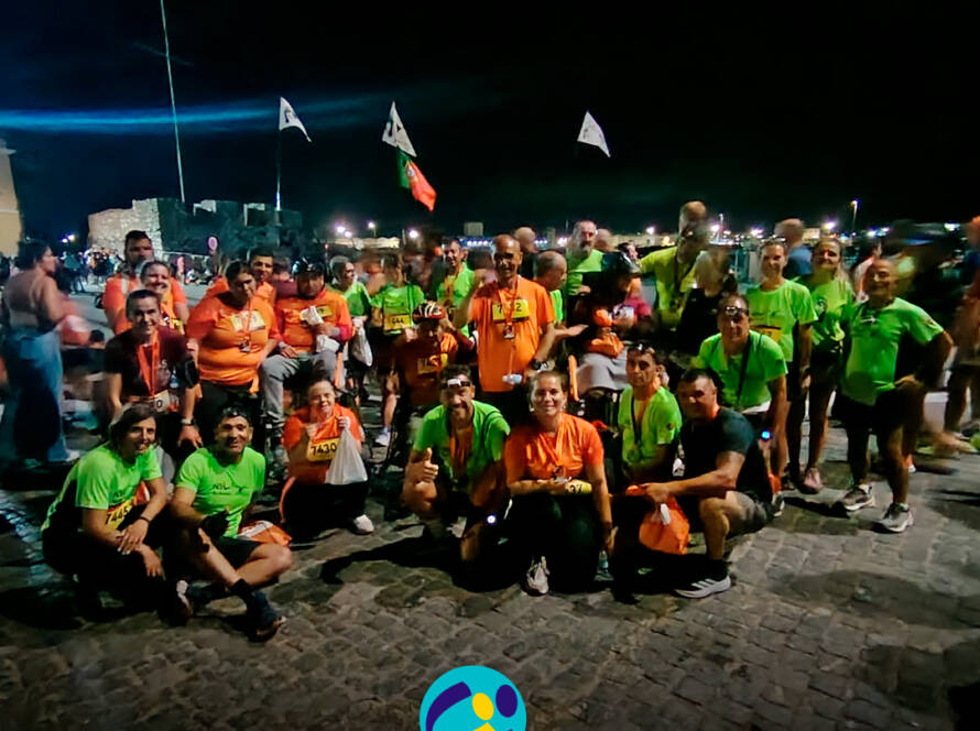 Grupo da Cercipeniche, acompanhado por voluntários da Equipa NEL, reúne-se no final da Corrida das Fogueiras para uma fotografia de grupo. Todos sorriem, exibindo as medalhas e celebrando a participação na prova. Logótipo da Cercipeniche.