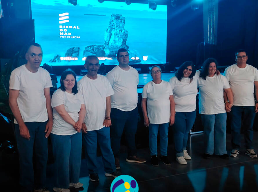 Fotografia de grupo com as pessoas apoiadas pela Cercipeniche antes da sua atuação na Bienal do Mar em Peniche. Logótipo da Cercipeniche.