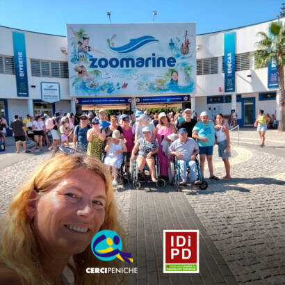 Grupo de pessoas apoiadas e monitores da Cercipeniche à entrada do Zoomarine, no Algarve. Logótipo da Cercipeniche e do IDiPD.