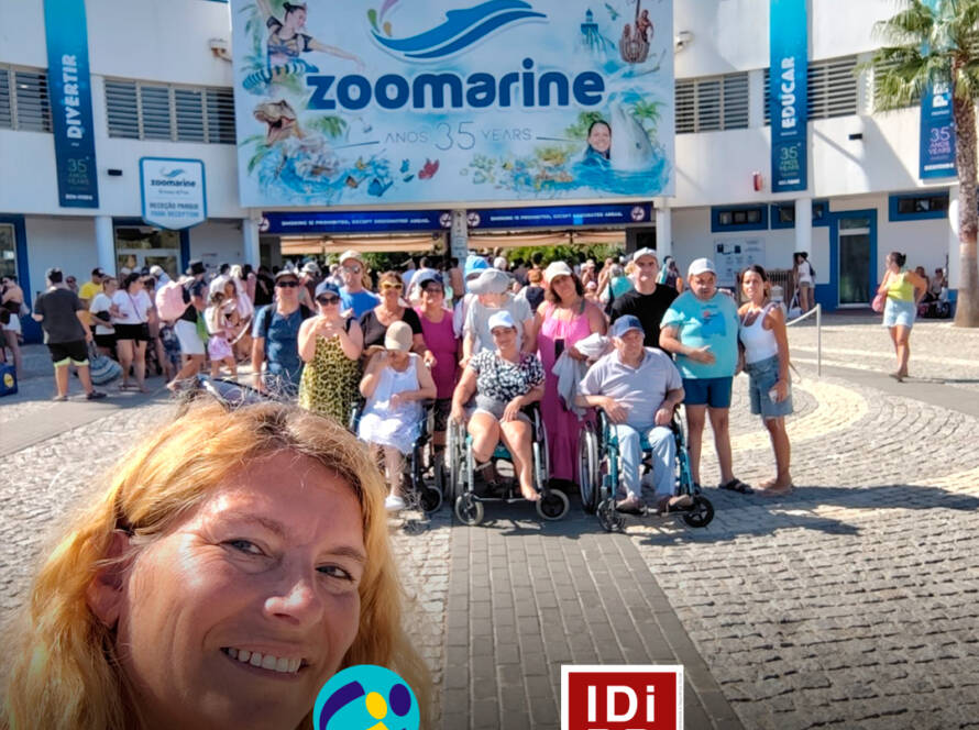 Grupo de pessoas apoiadas e monitores da Cercipeniche à entrada do Zoomarine, no Algarve. Logótipo da Cercipeniche e do IDiPD.