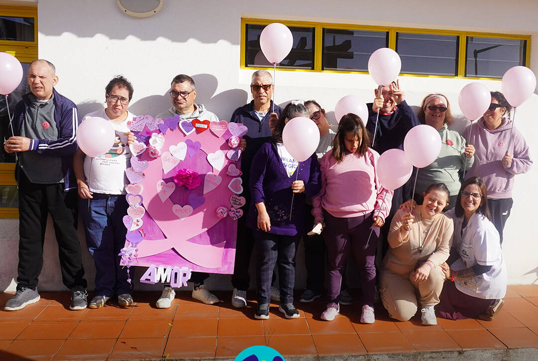 Grupo de pessoas apoiadas posa para uma fotografia no exterior do Cerisc. Várias pessoas seguram balões cor-de-rosa, enquanto outras apresentam o laço decorado com corações, flores, mensagens de sensibilização e um grande laço cor-de-rosa. Na parte inferior da imagem encontra-se o logótipo da Cercipeniche.