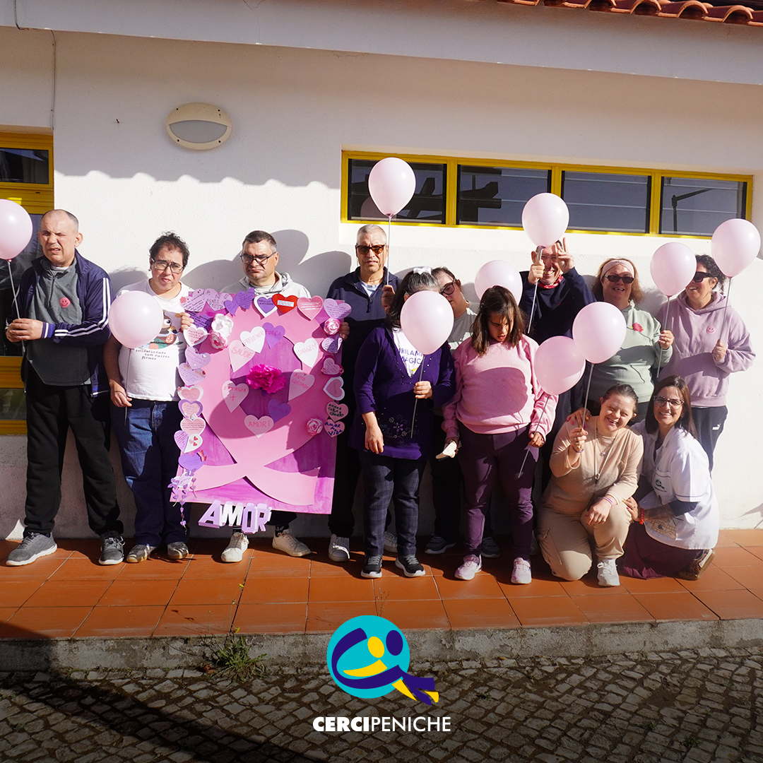 Grupo de pessoas apoiadas posa para uma fotografia no exterior do Cerisc. Várias pessoas seguram balões cor-de-rosa, enquanto outras apresentam o laço decorado com corações, flores, mensagens de sensibilização e um grande laço cor-de-rosa. Na parte inferior da imagem encontra-se o logótipo da Cercipeniche.