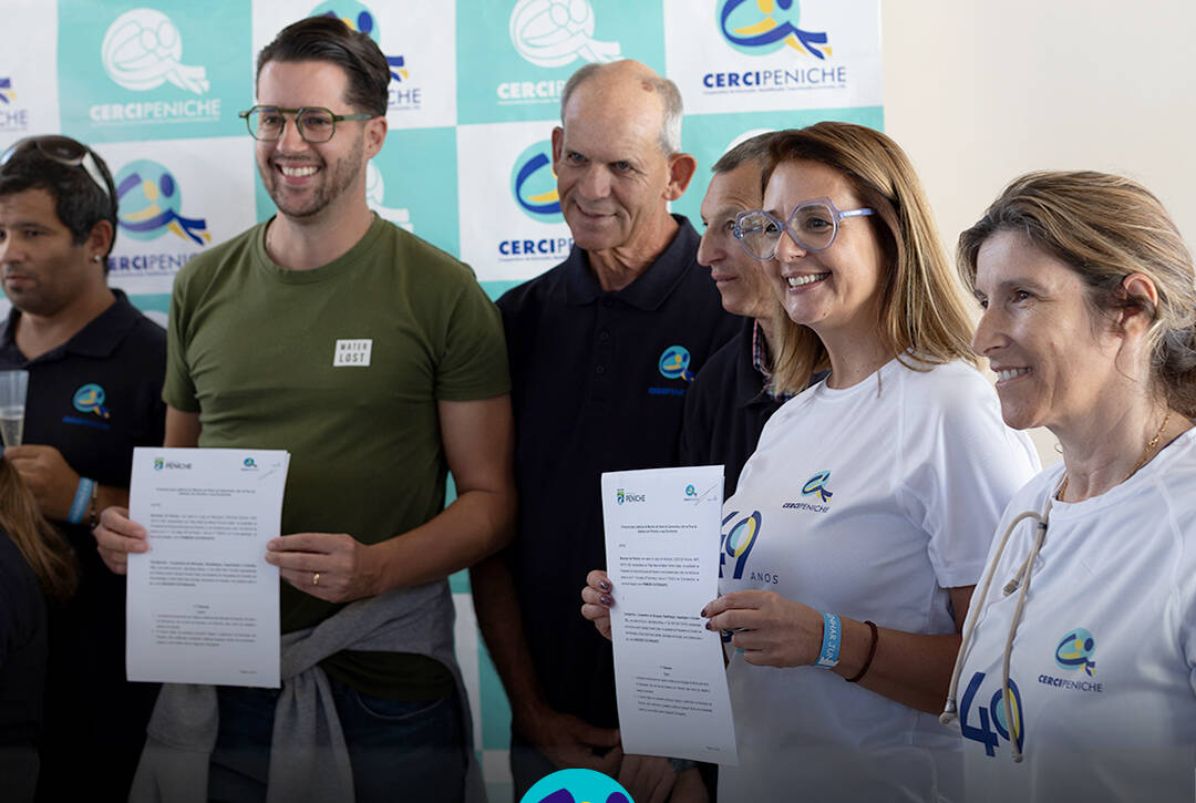 Grupo de seis pessoas posa para a fotografia em frente a um painel com os logótipos da Cercipeniche. Um homem de t-shirt verde e uma mulher com a t-shirt comemorativa dos 49 anos seguram documentos, enquanto os restantes participantes sorriem. Na parte inferior da imagem encontra-se o logótipo da Cercipeniche.