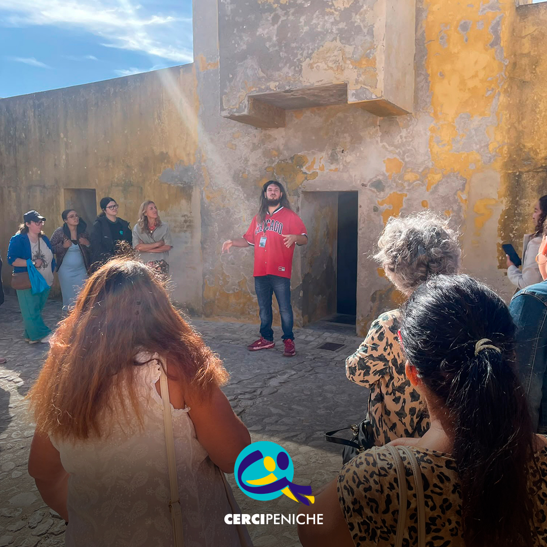 Dylan Almeida explica aos participantes diferentes aspetos do espaço e da sua história durante a visita guiada no exterior do Museu Nacional da Resistência e Liberdade. Na parte inferior da imagem encontra-se o logótipo da Cercipeniche.