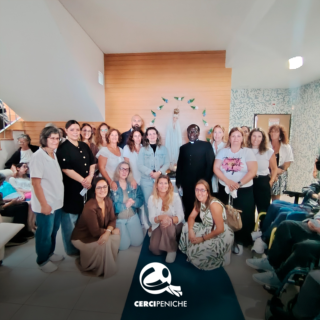 Um grupo de pessoas posa para uma fotografia no interior do Lar Porto de Abrigo, durante a visita de Nossa Senhora de Fátima Peregrina. Algumas pessoas estão de pé e outras agachadas. Ao centro encontra-se um sacerdote, vestido de preto, e ao fundo vê-se a imagem de Nossa Senhora. Na parte inferior da imagem encontra-se o logótipo da Cercipeniche.